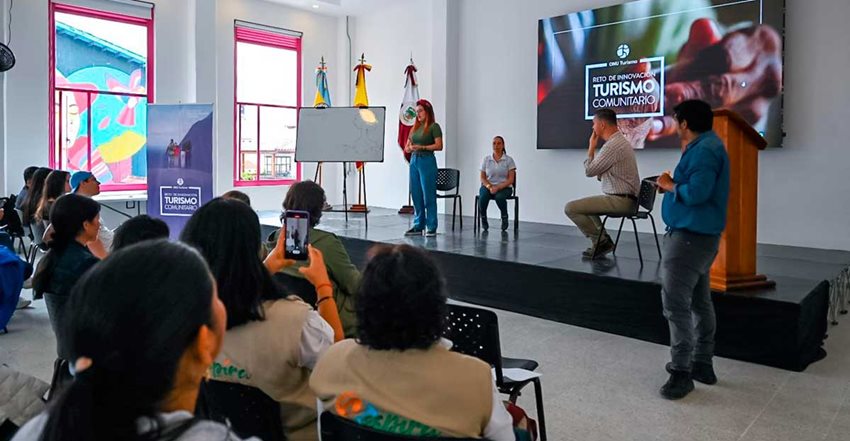 Mujer joven en el escenario de un salón, hablando al público.