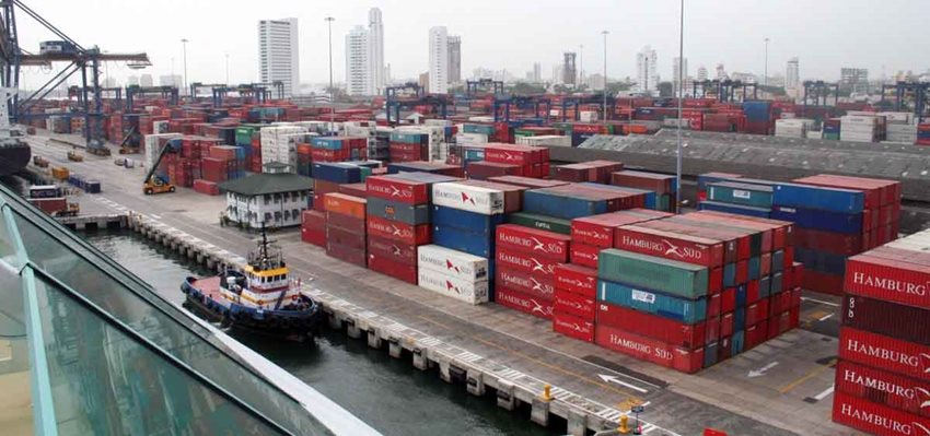 Contenedores de colores descargados en medio de una vía de zona franca y al lado pequeño barco.