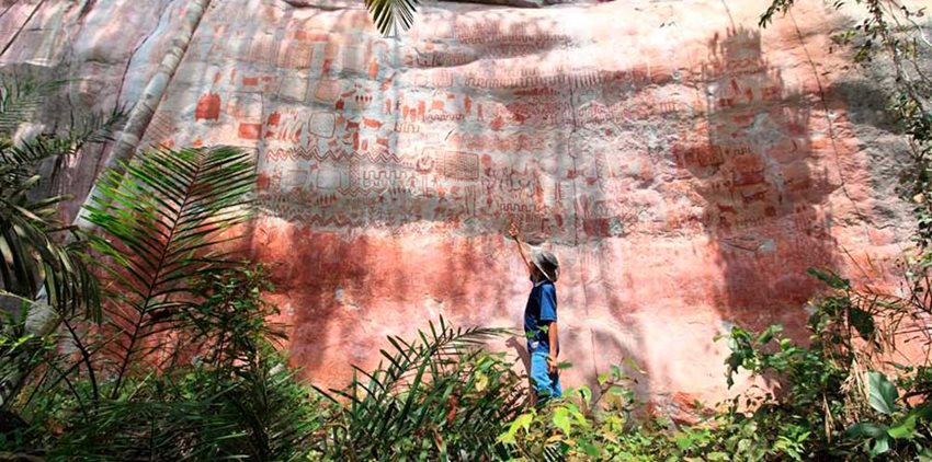 Descripción de la imagen: Hombre en medio del campo señalando pinturas rupestres en una roca.