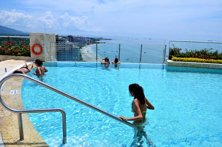 Mujeres dentro de una piscina en el último piso de un hotel con vista al mar.