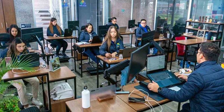 Hombres y mujeres, con chaquetas azules, sentados frente a computadores estudiando.