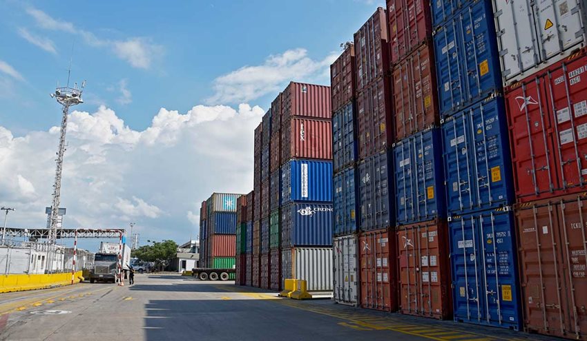 Contenedores de colores descargados en medio de la calle de un puerto, junto a un camión parqueado.