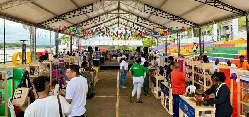 Descripción: Personas con stands y sus productos a la venta, bajo una carpa blanca.