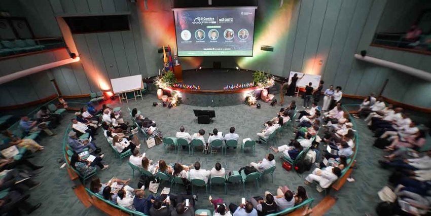Panorámica de auditorio y escenario, con personas sentadas esperando al ponente.