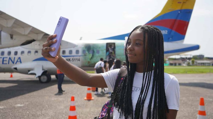 Descripción de la imagen: Niña morena tomándose una selfie al lado de un avión.
