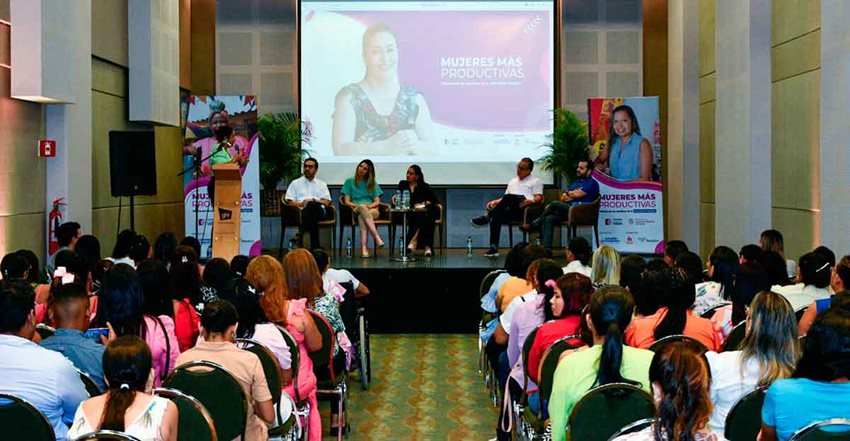 Personas en auditorio prestando atención a la exposición de los ponentes en el escenario.