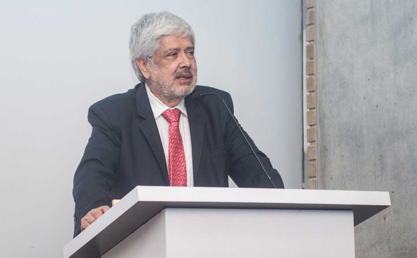 Ministro Germán Umaña con traje y corbata roja, sobre un atril dando una charla.