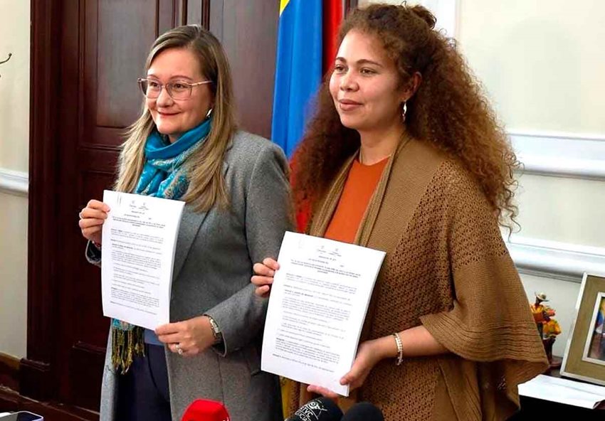 Dos mujeres sosteniendo sus documentos en las manos y posando para la foto, de pie.