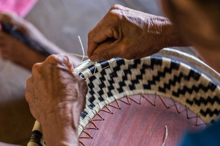 Manos de artesano tejiendo.