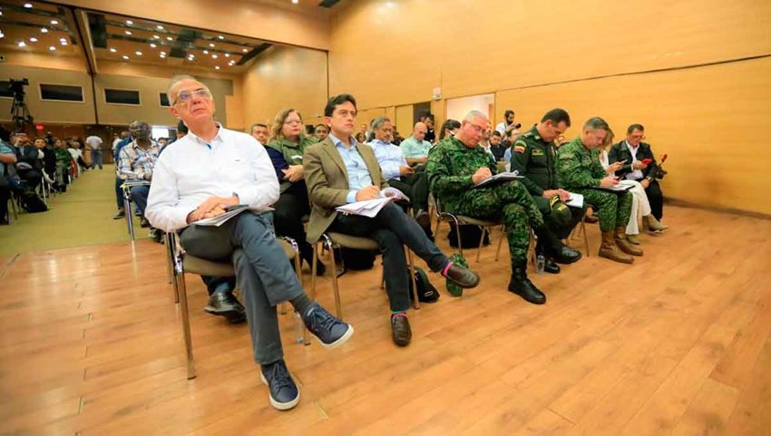 Militares y funcionarios del Gobierno sentados prestando atención a alguien hablando en el escenario.