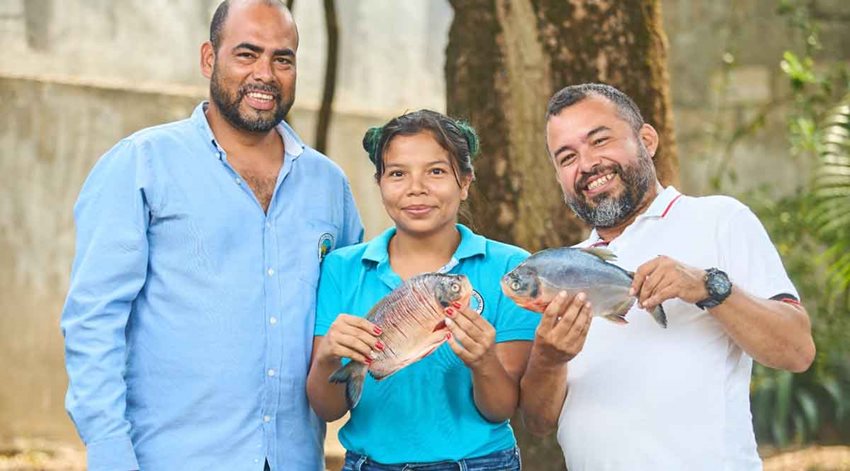 Dos hombres y una mujer posando con pescados en las manos.