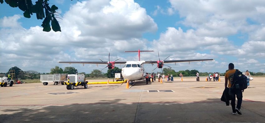 Fotografía de frente de avión parqueado mientras se suben los pasajeros por la parte de atrás.