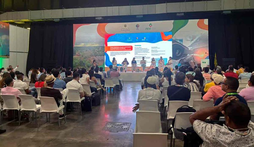 Personas poniendo atención a expositores en el escenario.