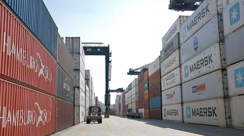 Calle de zona franca con contenedores de colores descargados y máquina de carga parqueada.