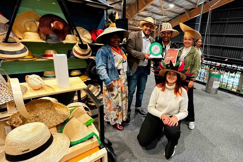 Descripción de la imagen: Hombres y mujeres posando para la foto con sombreros artesanales puestos.