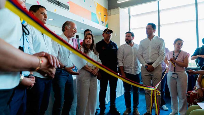 Hombres y mujeres sosteniendo cinta, con la bandera de Colombia, para inaugurar evento.