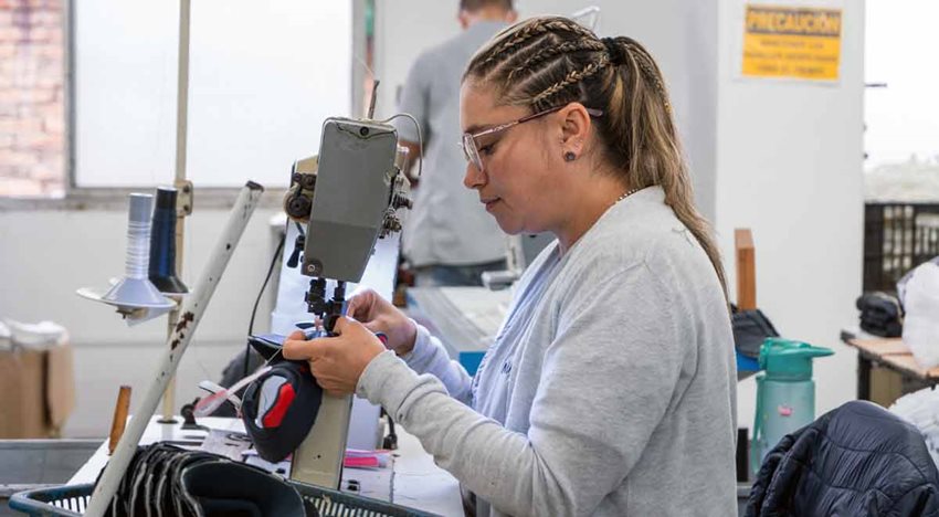 Mujer frente a máquina industrial cosiendo unas prendas.