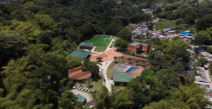 Descripción: Foto panorámica de casas, edificios y canchas en medio de la naturaleza.