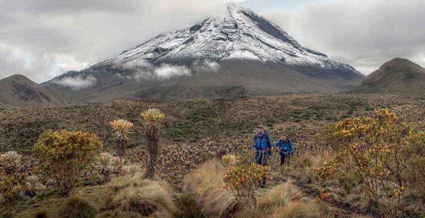 Hombre y mujer caminando en medio de un páramo y un nevado al fondo.