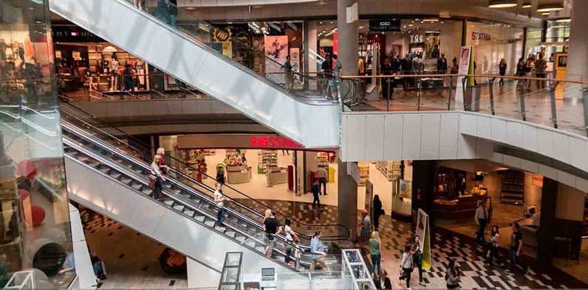 Personas caminando por pisos de un centro comercial, usando las escaleras eléctricas.