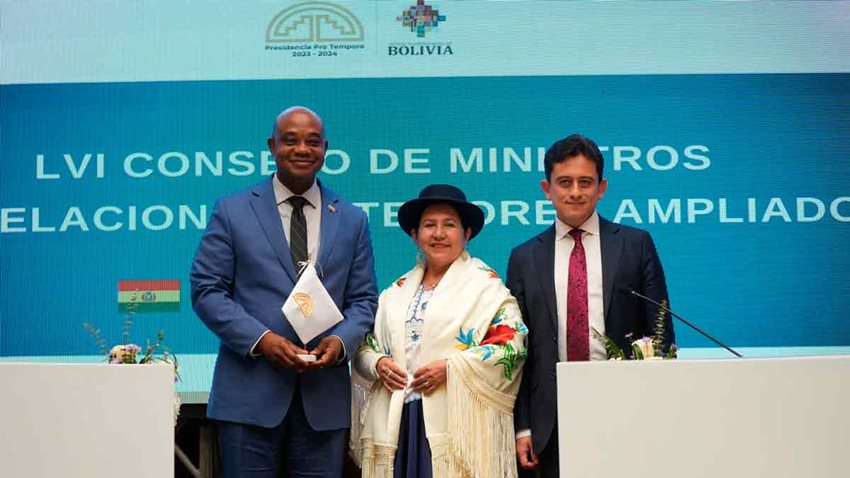 Dos hombres de traje y en el medio una mujer con vestido típico de Bolivia, posando los tres para la foto.