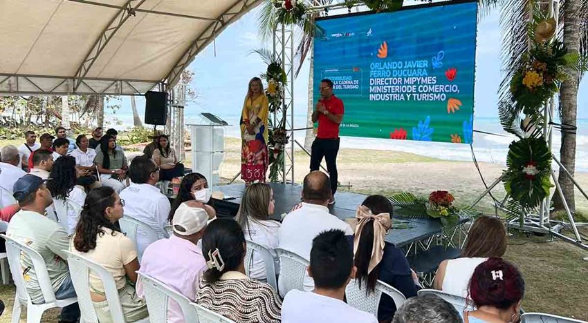 Hombre, con camisa roja, hablando por micrófono al público desde el escenario.