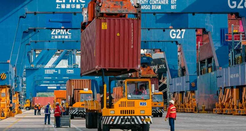 Camiones amarillos cargando contenedores vinotinto en medio de calle de zona franca.