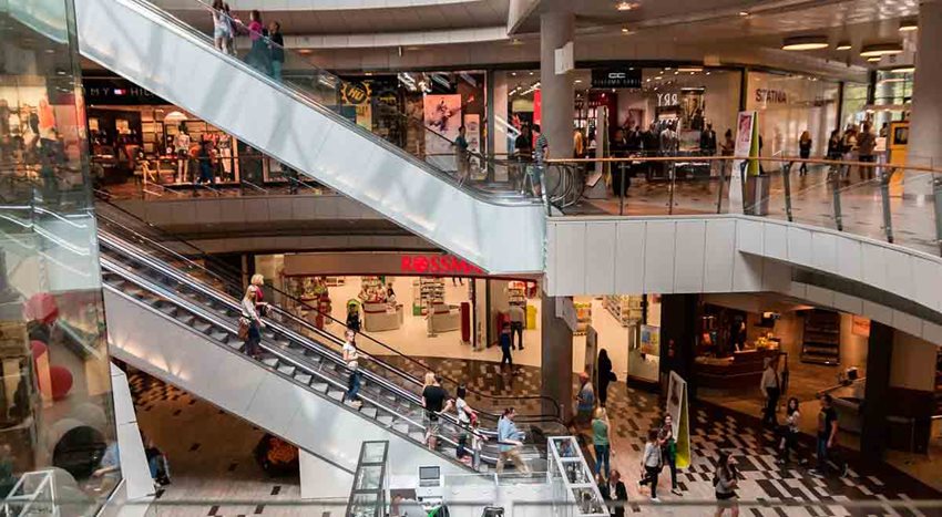 Foto panorámica de centro comercial al interior, donde se ve gente caminando y las escalera eléctricas.