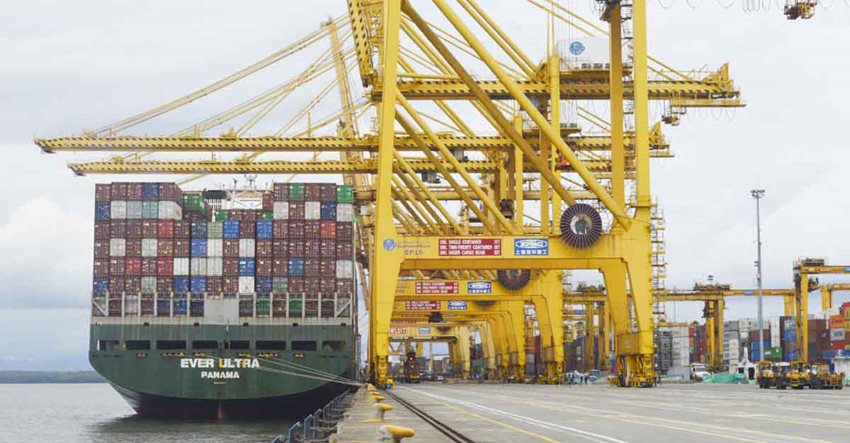 Barco cargado de contenedores de colores, estacionado en puerto con estructuras amarillas.