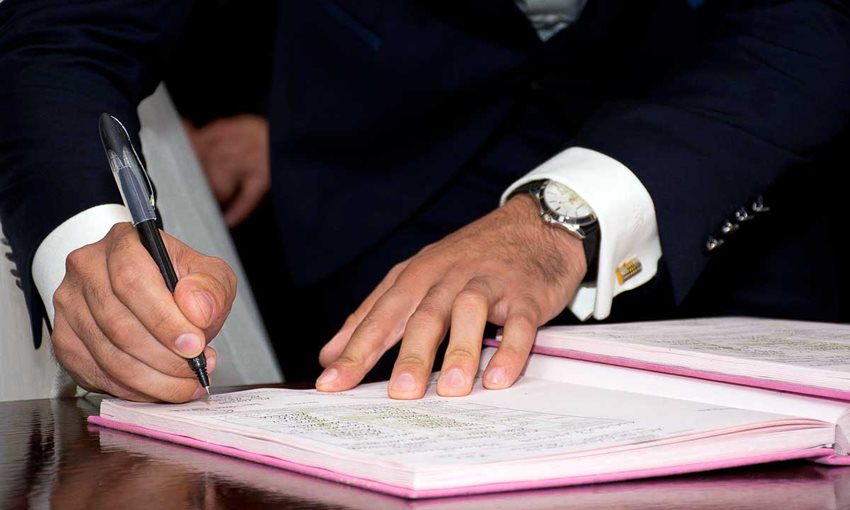 Manos de hombre con traje firmando un documento en un libro.
