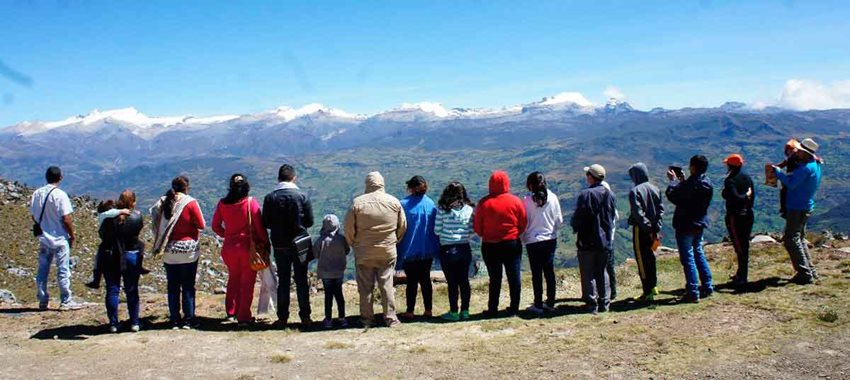Hombres, mujeres y niños posando de espaldas y viendo hacia un paisaje de montañas.