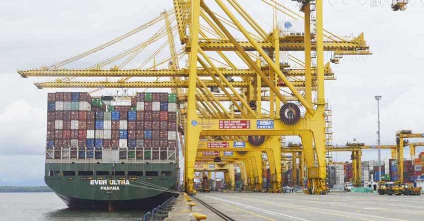 Barco cargado de contenedores de colores, estacionado en puerto con estructuras amarillas.