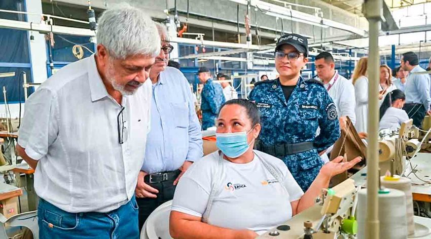 Ministro Umaña hablando con mujer que está trabajando en máquina de coser.