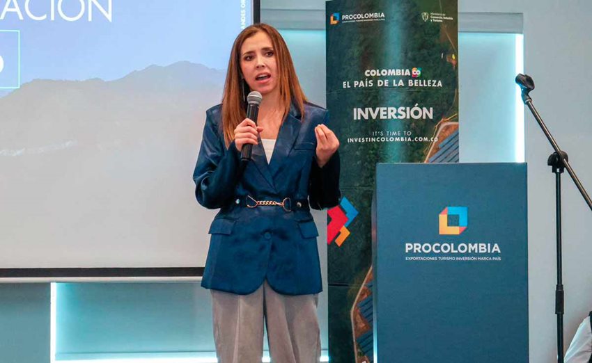 Mujer, de pie, hablando por micrófono al público desde el escenario.