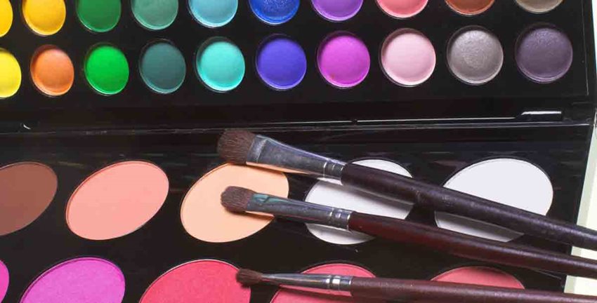 Tres brochas para maquillaje, de diferentes tamaños, sobre paleta de colores de sombras y rubor.
