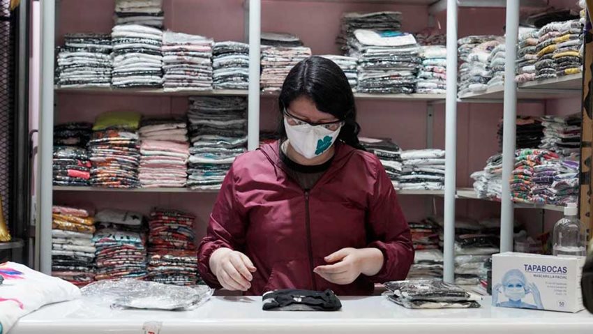 Microempresaria, con tapabocas, organizando los productos de su negocio.