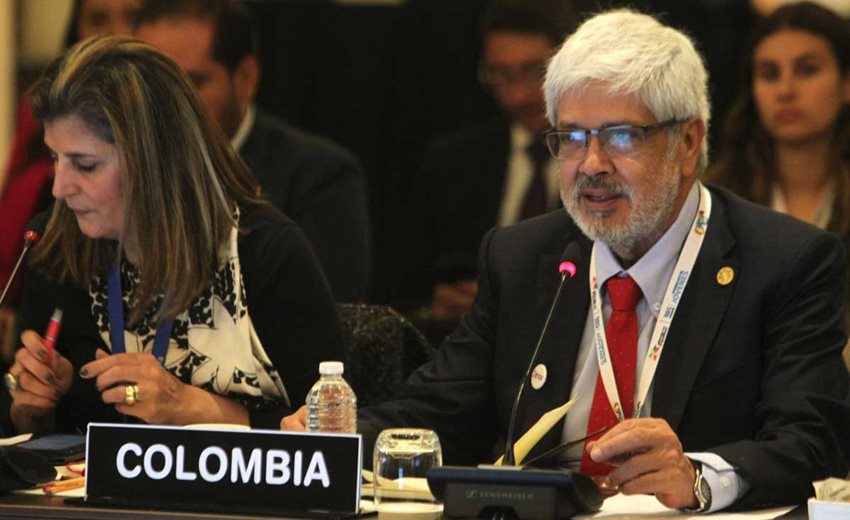 Ministro Germán Umaña, sentado al lado de una mujer y frente a un micrófono, hablando al público.