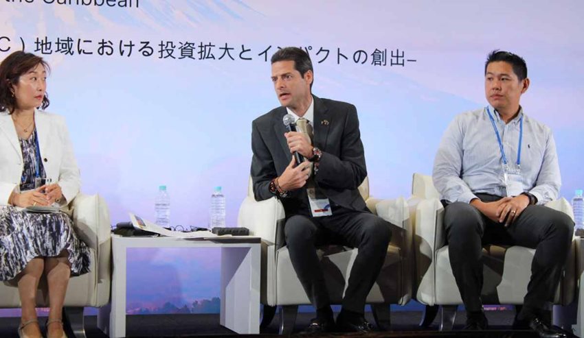 Ministro hablando por micrófono en medio de una exposición en un evento en Japón.