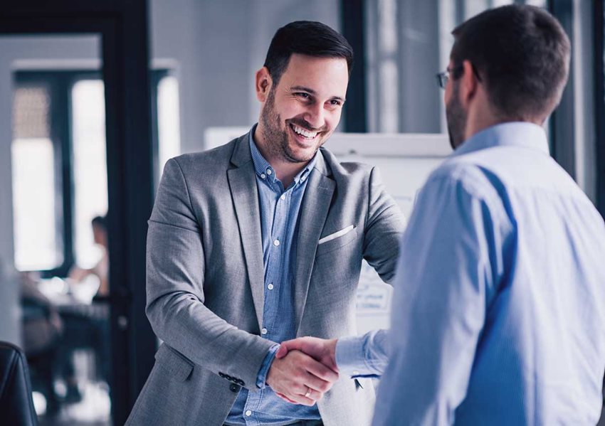 Dos hombres con traje, en la oficina, dándose la mano.