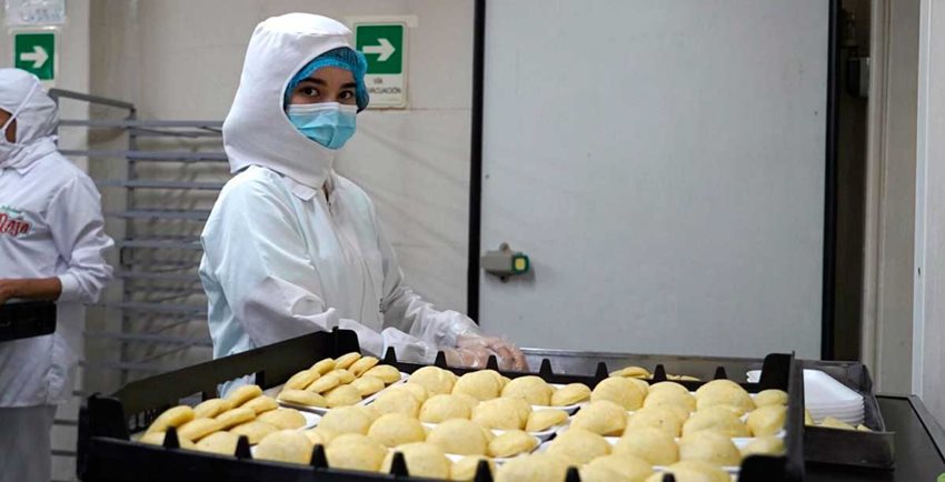 Mujer con traje blanco higiénico y tapabocas manipulando empanadas.