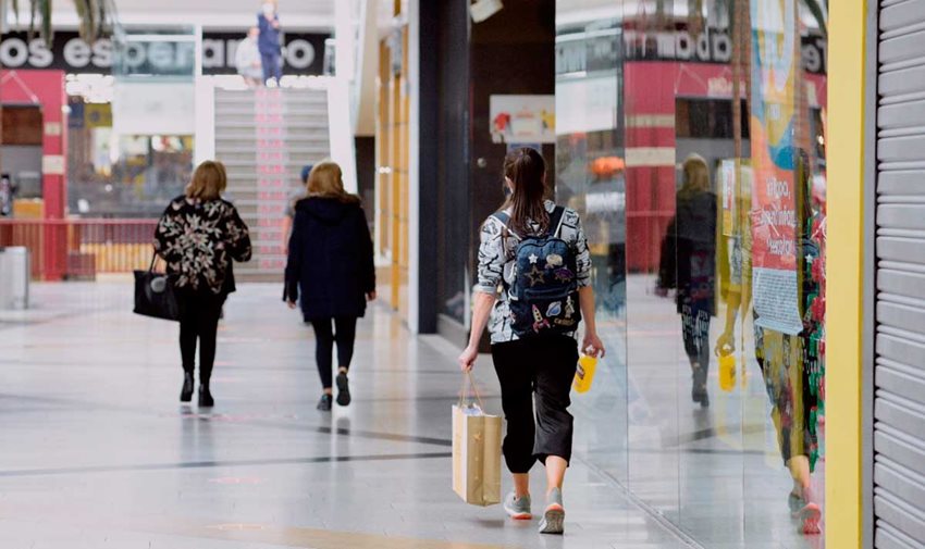 Mujeres, de espalda, caminando por centro comercial con bolsas en las manos.