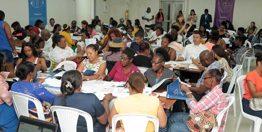 Hombres y mujeres sentados frente a unas mesas leyendo documentos.