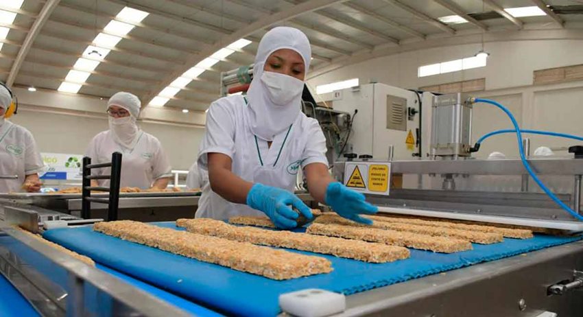 Mujer, con traje blanco de seguridad e higiene, manipulando alimentos en fábrica.