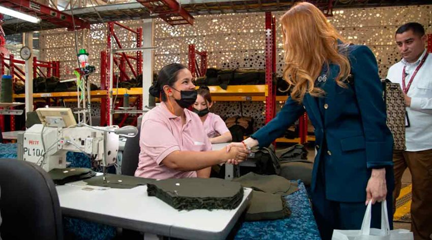 Ministra Diana Morales saludando a mujer en su puesto de trabajo en fábrica de confecciones.