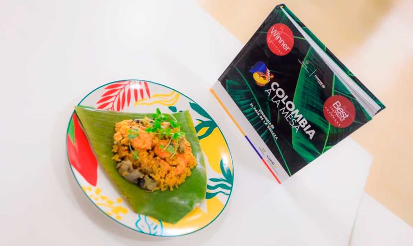 Plato colorido con comida de arroz con camarones y al lado el libro 