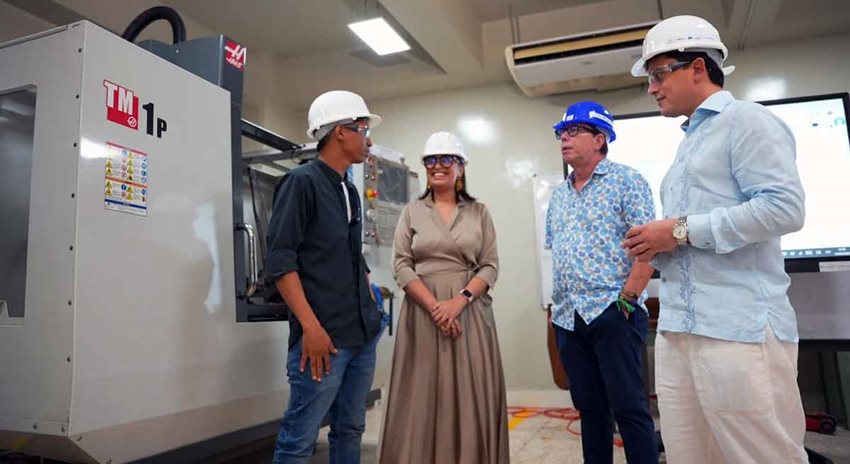 Tres hombres y una mujer, con equipos de seguridad dentro de una planta, conversando al lado de una máquina.