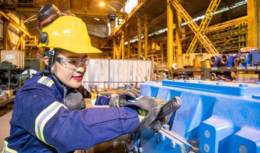 Mujer, con elementos y ropa de seguridad, manipulando una máquina en una planta.
