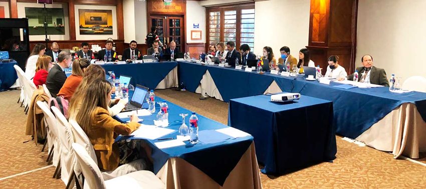 Hombres y mujeres sentados en tres mesas, en forma de U, hablando durante una reunión.