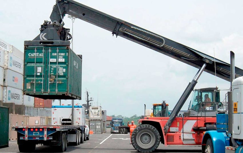 Máquina cargando un contenedor verde para ubicarlo sobre el tráiler de un camión.