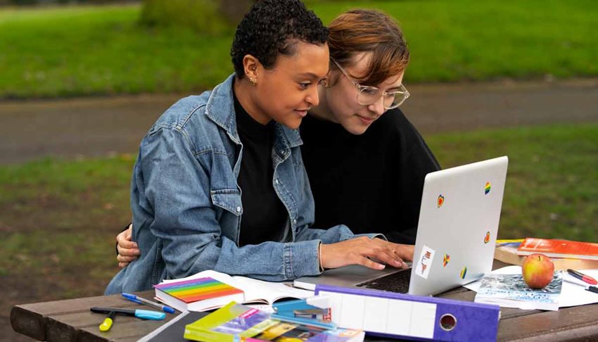 Dos mujeres abrazadas y sentadas, viendo un computador portátil blanco.
